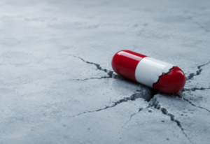 Cracked red and white capsule on fractured concrete representing mitragynine pseudoindoxyl (pseudo) drug risks and addiction dangers.